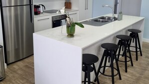 Eine moderne Küche mit weißen Schränken, einem Edelstahlkühlschrank, einer zentralen Kochinsel mit Sitzgelegenheiten und einer Spüle.