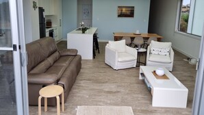 Ein modernes Wohnzimmer mit einer braunen Ledersofa, weißen Sesseln, einem Holztisch und einem Essbereich mit einem Holztisch und Stühlen.