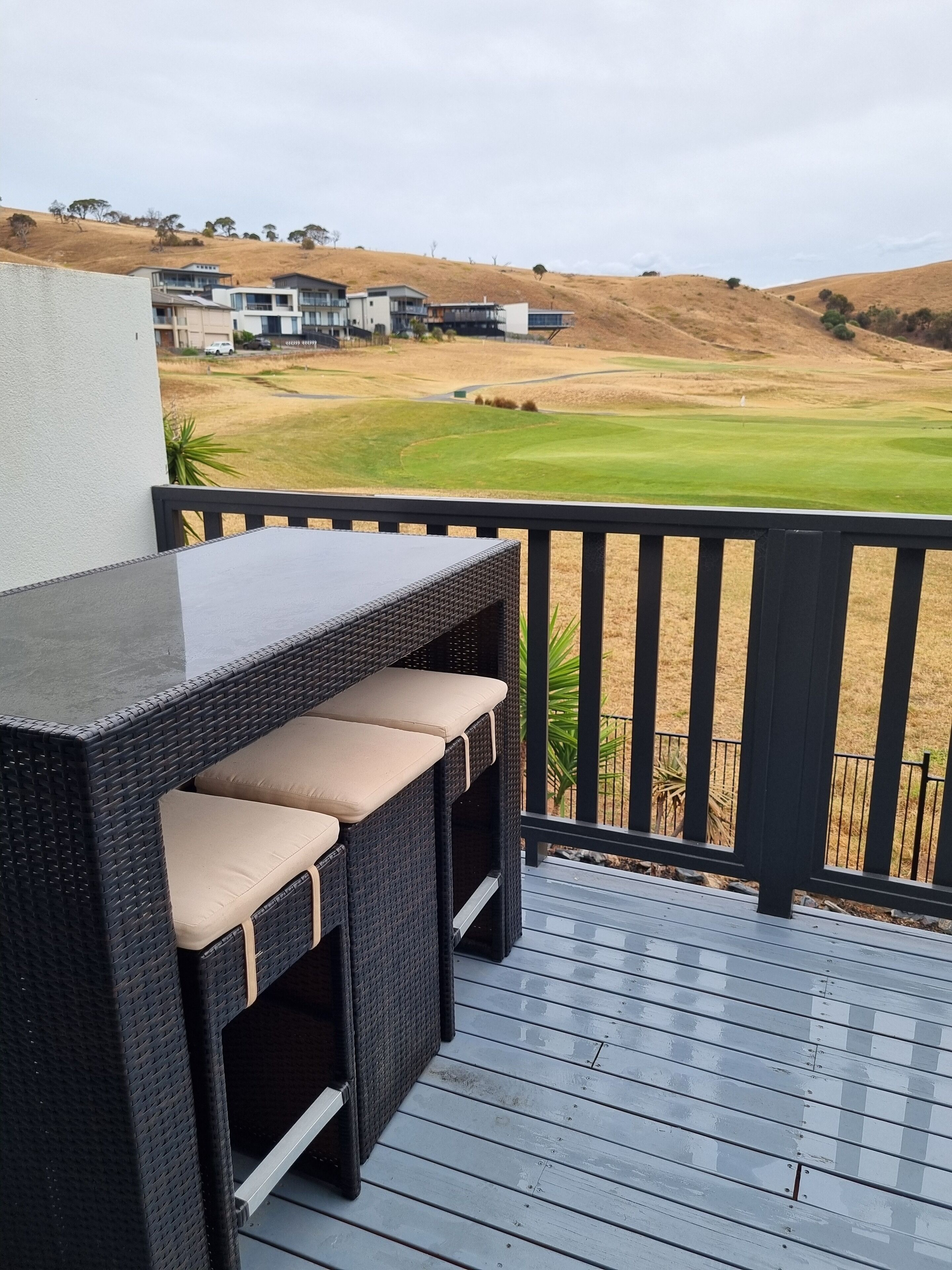 A deck with a table and chairs, overlooking a golf course.