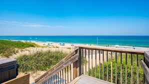 Eine Holzterrasse mit Blick auf einen Strand unter blauem Himmel.