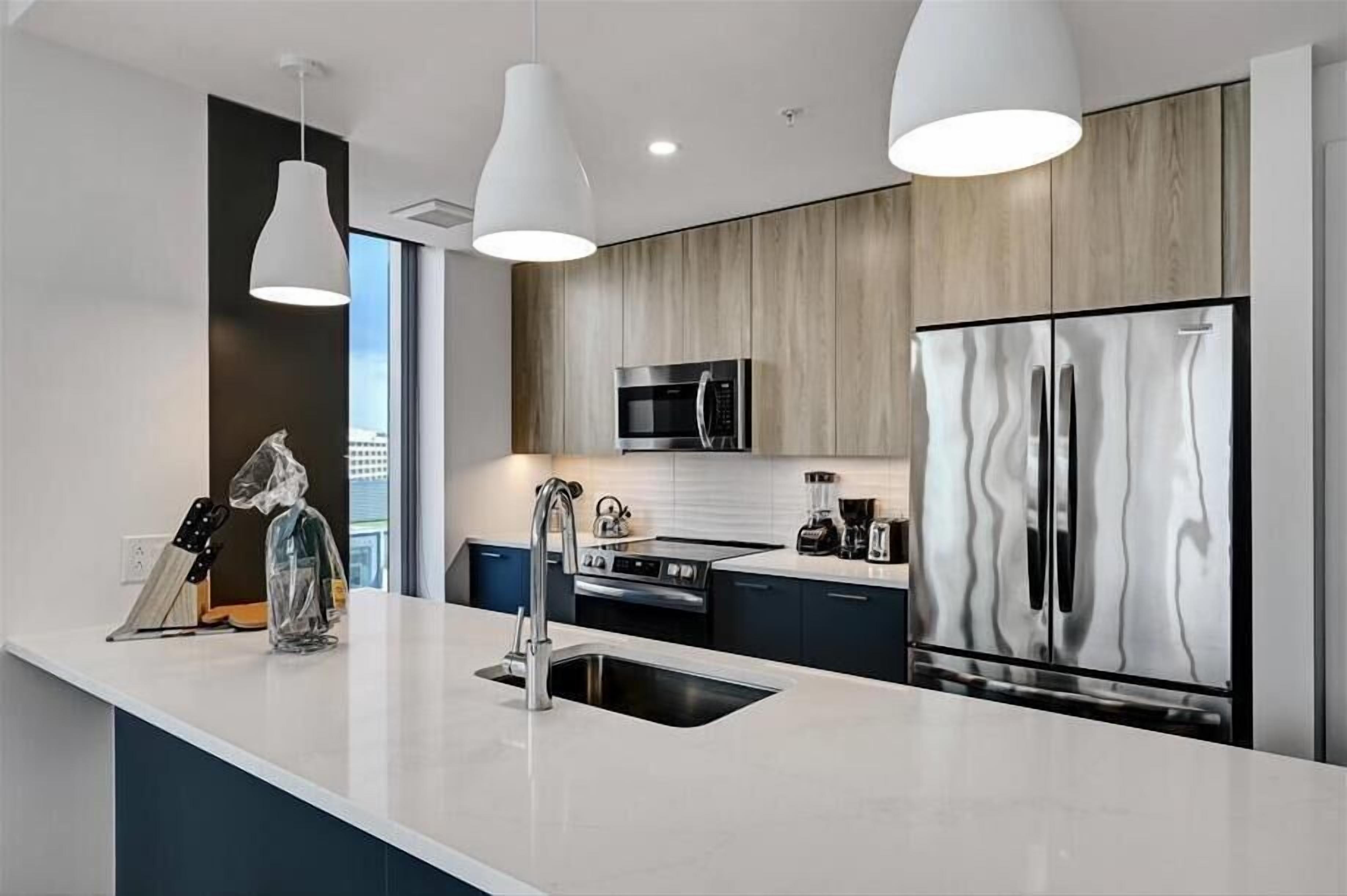 A modern kitchen with a large island, stainless steel appliances, and pendant lighting.