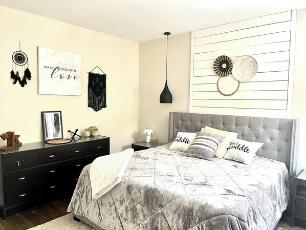 Une chambre à coucher avec une tête de lit capitonnée grise, une couvre-lit matelassée grise et deux tables de chevet ornées d’objets décoratifs.