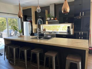 Une cuisine moderne dotée d’un grand îlot central, de tabourets de bar en acier inoxydable et de luminaires suspendus.