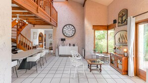 A spacious living area with a wooden staircase, a vintage clock, and a view of greenery outside. - Beautiful home in Meyzieu (Meyzieu)