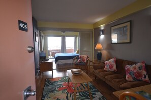 Habitación de hotel con cama, sofá, sillón, mesa y un amplio ventanal.