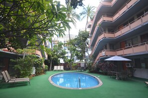 Un área de piscina con césped artificial, sillas de descanso y una mesa con sombrilla.
