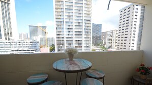 Un balcón con una mesa redonda y cuatro taburetes, con vistas a un paisaje urbano con edificios altos.