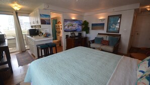 Habitación de hotel con una cama grande, un escritorio con una computadora, un televisor y vistas al balcón exterior.