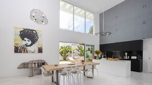 A modern kitchen with a black countertop and white cabinets, a dining area with a wooden table and white chairs, and a large window overlooking a garden. - Villa Glamour / Villa with pool (Aroeira)