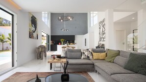 A modern living room with a sectional sofa, a glass coffee table, and a dining area with a kitchen in the background. - Villa Glamour / Villa with pool (Aroeira)