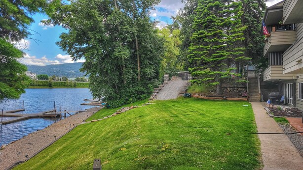 A residential property with a well-maintained lawn, a dock by the lake, and a stone staircase leading to a deck. - Waterfront Condo AC Boat Slip Downtown  (Sandpoint)