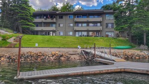 A multi-story building with balconies, a dock, and a grassy area. - Waterfront Condo AC Boat Slip Downtown  (Sandpoint)