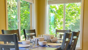 A dining room with a wooden table and chairs, large windows with blinds, and a ceiling fan. - Waterfront Condo AC Boat Slip Downtown  (Sandpoint)