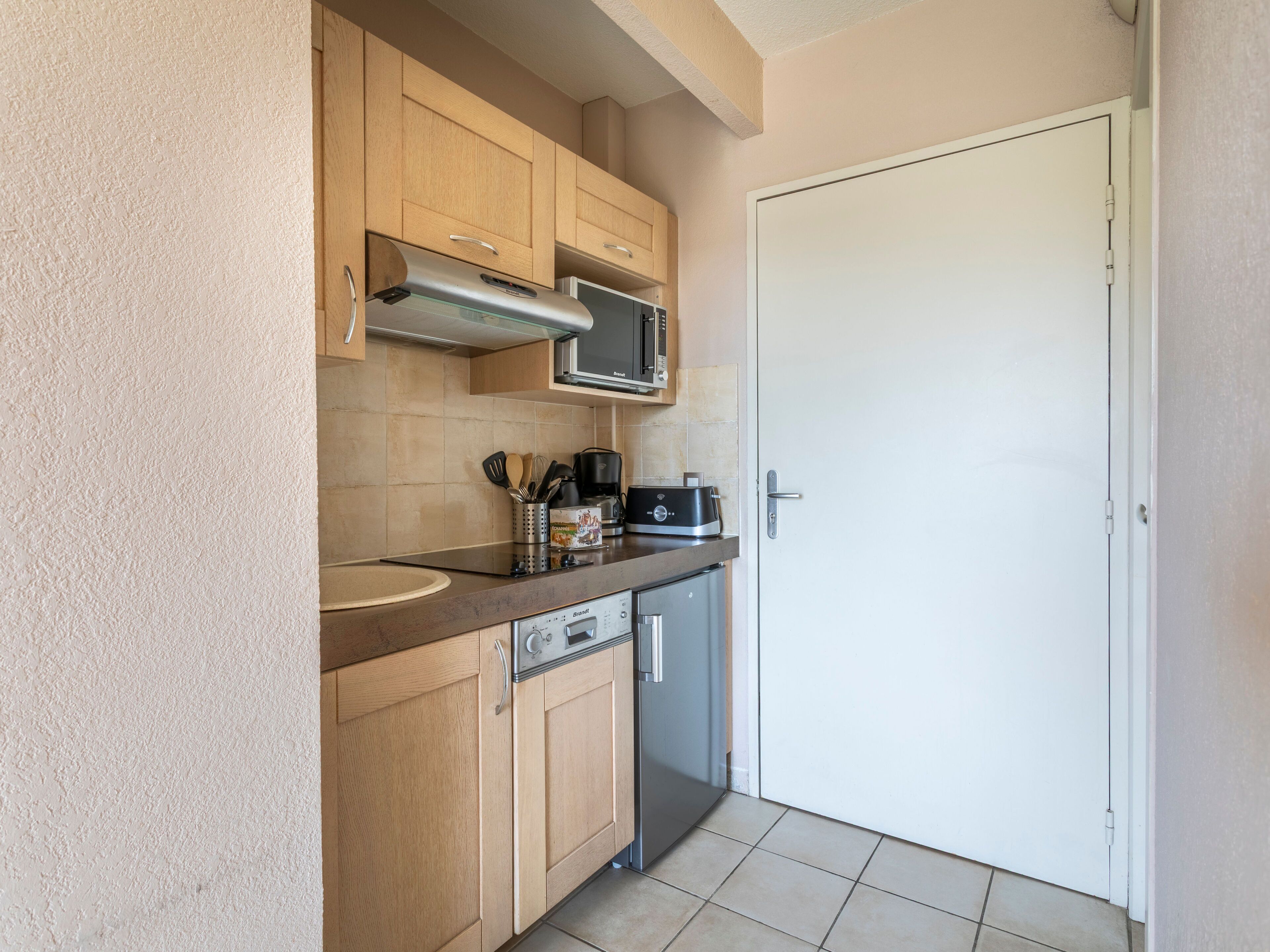 Cozinha compacta com armários de madeira, exaustor de aço inoxidável, micro-ondas e máquina de lavar louça.