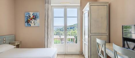 A hotel room with a bed, a desk, and a view of the outdoors.