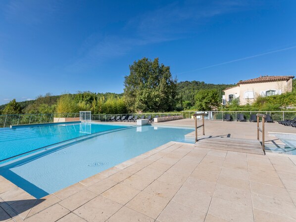 A swimming pool with a tiled deck, lounge chairs, and a view of a hillside with trees and a building.