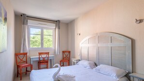 Una camera d'albergo con un letto, una scrivania, due sedie, una finestra con tende e una lampada a parete.