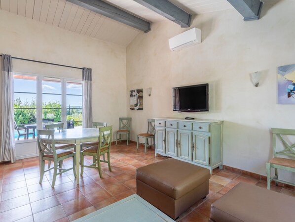A spacious living area with a dining table, chairs, a sofa, a TV, and a cabinet.