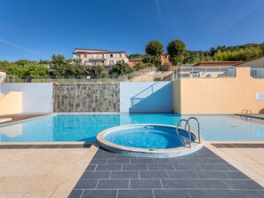 A swimming pool with a tiled deck, a stone wall, and a view of a building in the background.