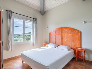 A bedroom with a large bed, a window with curtains, and a view of greenery outside.
