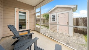 Une terrasse couverte avec deux fauteuils Adirondack, une terrasse en bois et une vue sur une maison avec un garage et une clôture en bois.