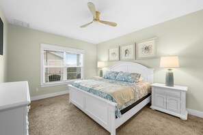 A bedroom with a bed, two bedside tables, a ceiling fan, a window with blinds, and wall art.