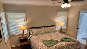 Ein Schlafzimmer mit einem Bett, zwei Nachttischlampen, einem Deckenventilator und einer Tür zu einem Badezimmer.