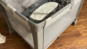 Ein grauer Babywippstuhl mit Netzmaterial an der Seite und gepolstertem Sitz, ausgestattet mit einem Griff und einem anhängenden Spielzeug.