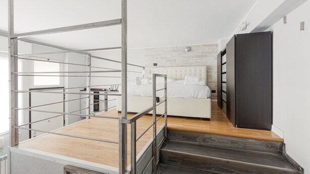 Decoração moderna com escada que dá para um quarto, corrimão metálico e cama branca.