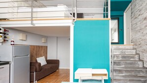 Um apartamento moderno com cozinha, um sofá marrom, uma parede de destaque verde-azulado e uma escada.