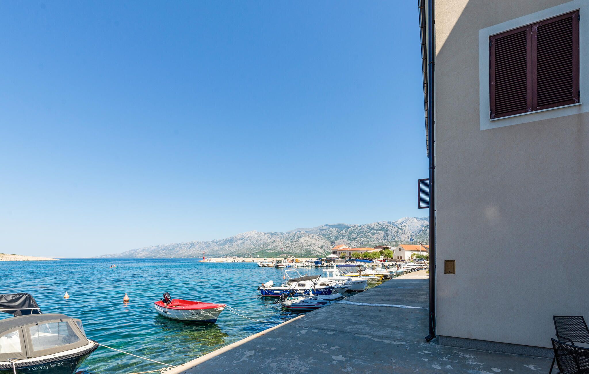 Un port de plaisance avec des bateaux amarrés, un ciel bleu azur et une chaîne de montagnes en arrière-plan.