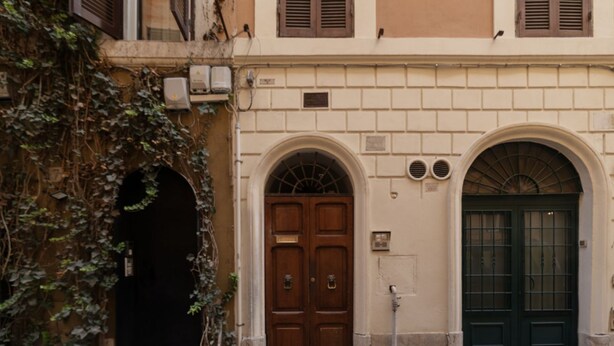 A building with a central arched doorway, a smaller arched window, and a green door with a barred design.