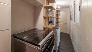 A kitchen with a stove, wooden shelves, and a tiled backsplash.