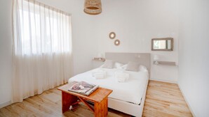 A bedroom with a bed, bedside tables, a hanging light, a window with curtains, and a wall-mounted mirror.