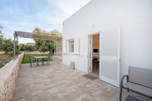 Une terrasse avec une table et des chaises, une pergola et un mur extérieur blanc.
