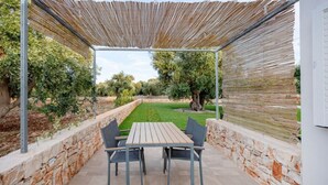 An outdoor patio with a table and chairs, stone walls, and a view of a garden. - GuestHost - Cozy apartment that accommodates 5 people, located in the quiet countryside of Monopoli, in a villa surrounded by one hectare of centuries-old olive trees. The accommodation, with parking included, offers large open spaces, a patio with barbe (Monopoli)