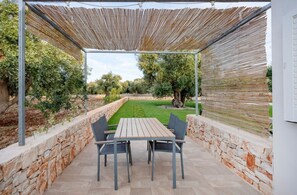 An outdoor patio with a table and chairs, stone walls, and a view of a garden.
