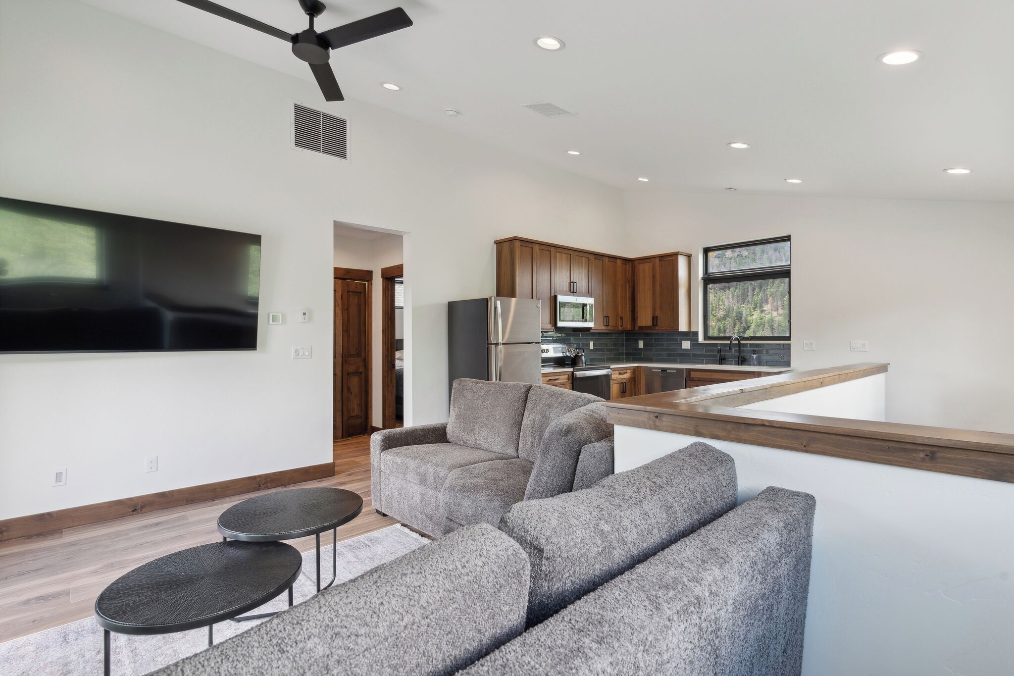 A modern living room with a grey sectional sofa, a small round table, and a flat-screen TV mounted on the wall.