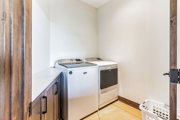 A laundry room with a washer and dryer, wooden cabinets, and a white laundry basket. - Durango Luxury-Stunning Views! Easy to Town or Ski (Durango)