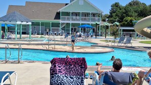 A pool area with lounge chairs, a building with a balcony, and a water slide.