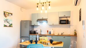 A modern kitchen with a dining area, featuring a wooden table, chairs, and a hanging light fixture.
