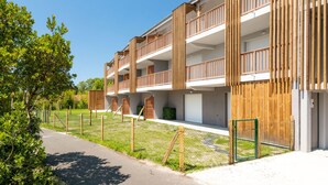 A modern multi-story building with balconies, a paved pathway, and a fenced garden area.