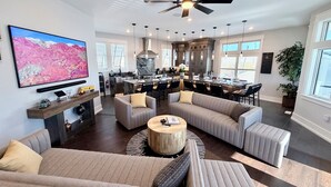 Amplia sala de estar con un televisor de pantalla plana grande, chimenea y cocina moderna con gabinetes oscuros y una isla de mármol.