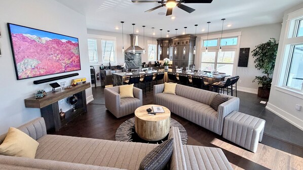 Amplia sala de estar con un televisor de pantalla plana grande, chimenea y cocina moderna con gabinetes oscuros y una isla de mármol.