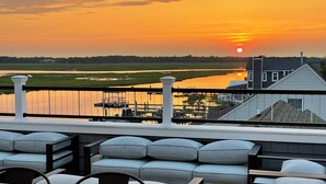 Una terraza con mobiliario y vistas a la puesta de sol sobre el agua.