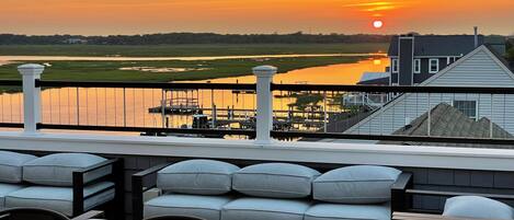 Una terraza con mobiliario y vistas a la puesta de sol sobre el agua.