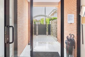 A hotel entrance with a glass door, a brick wall, a metal gate, and a wall-mounted umbrella holder.