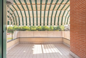 Un balcone coperto con un tenda a righe, pavimento piastrellato e parete in mattoni.