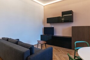 Un salon moderne avec un canapé, une petite table, un téléviseur fixé au mur et un fauteuil vert.