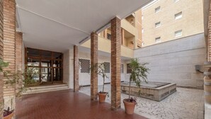 A courtyard with brick flooring, potted plants, and a building entrance with a glass door. - GuestHost - Comfortable apartment located on the seventh floor, of nine in total, equipped with a lift (NOT suitable for disabled people). There are steps at the entrance.In 65 m2 of space it accommodates 2 people with a double bedroom.The location is ex (Roma)